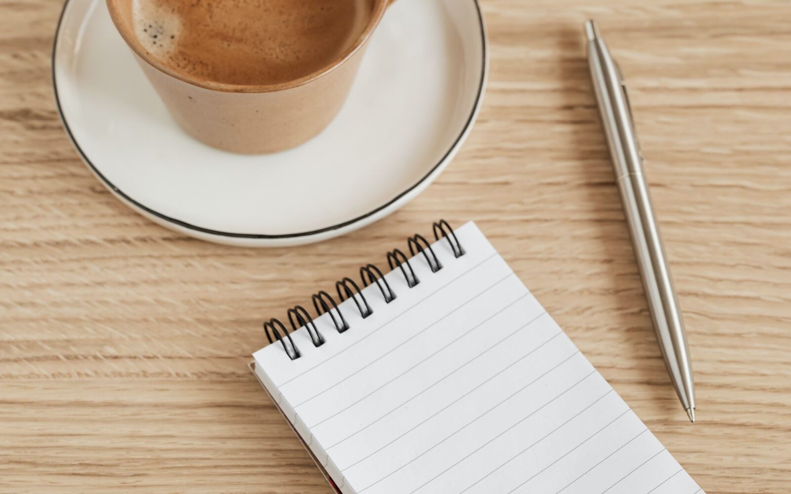 Carnet, stylo et tasse de café posés sur une table en bois