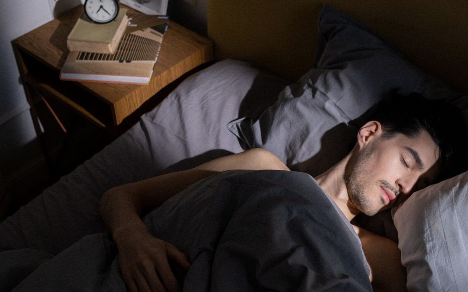 Chambre au petit matin, personne endormie et réveil posé sur la table de nuit
