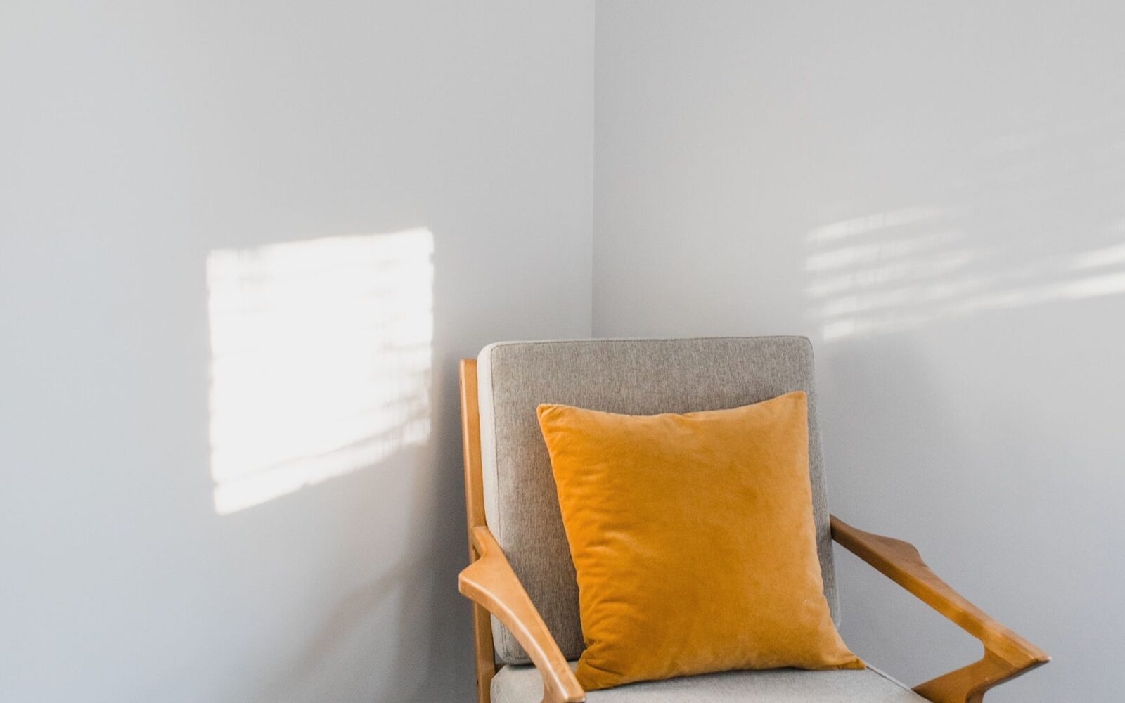Fauteuil clair avec un coussin ocre dans un angle de pièce éclairé par la fenêtre