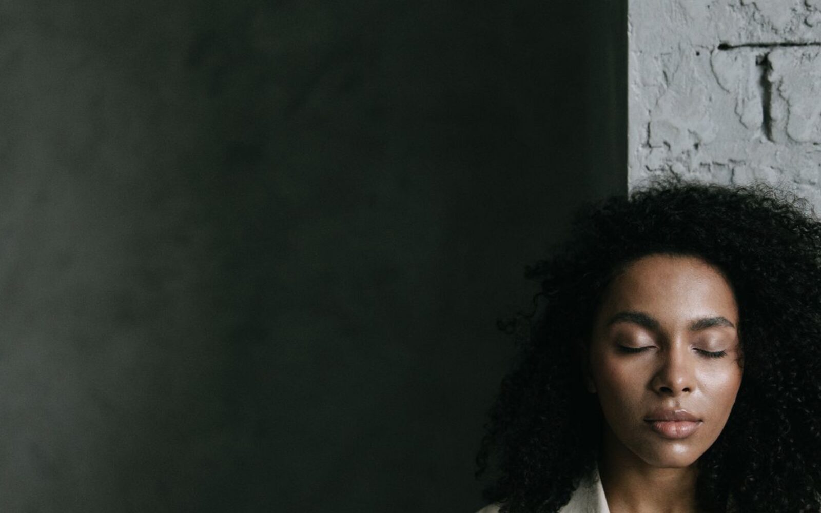 Femme adossée à un mur clair, les yeux fermés, dans une lumière douce
